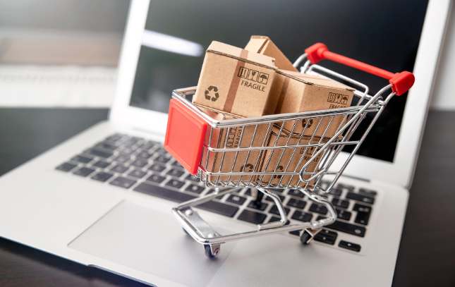 Figurka wózka zakupowego z kartonikami postawiona na laptopie
