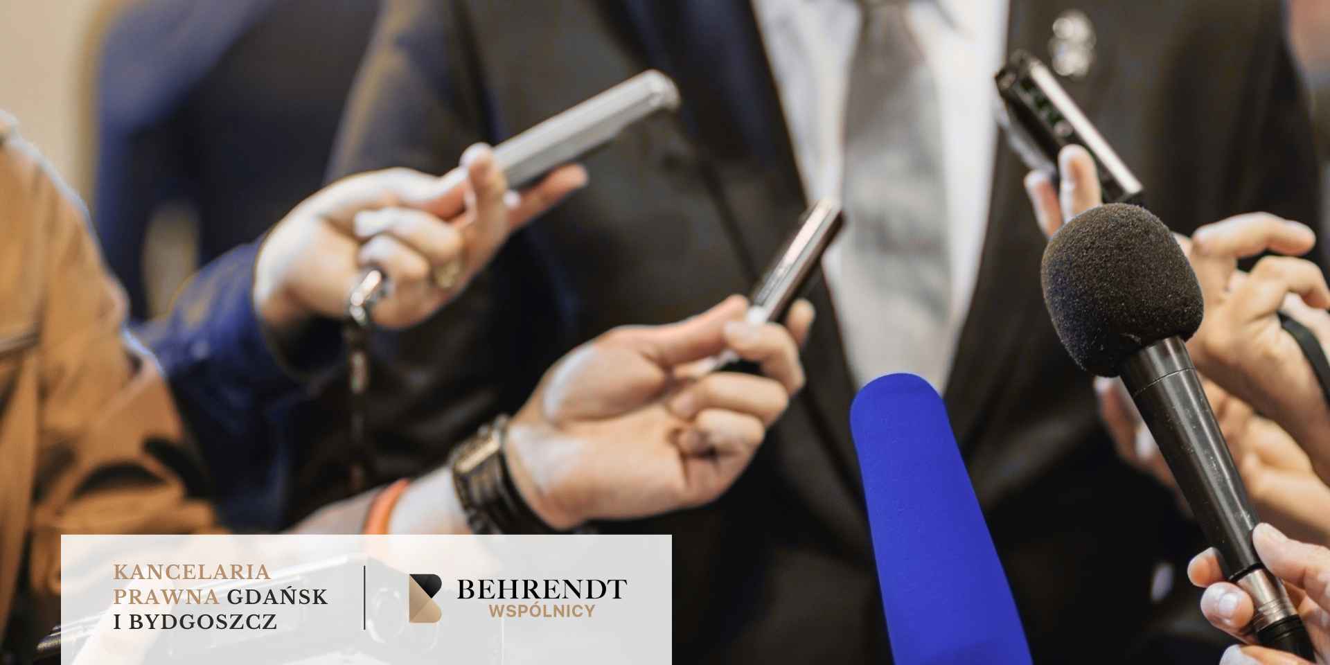 <br />
Podczas konferencji prasowej, osoba w garniturze stoi otoczona mikrofonami i dyktafonami trzymanymi przez dziennikarzy