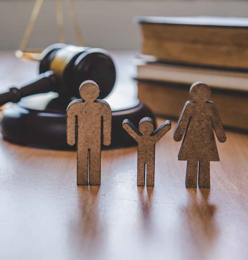 <br />
Na drewnianym stole stoją trzy drewniane figurki symbolizujące rodzinę, a w tle widać młotek sędziowski, stos książek i szalę wagi