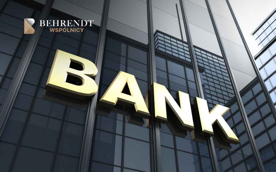 Zbliżenie przedstawia duże, złote litery tworzące napis BANK na ciemnej, nowoczesnej fasadzie przeszklonego budynku