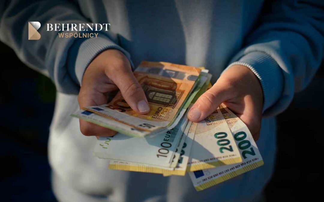 Dłonie trzymają wachlarz banknotów euro, w tym o nominałach 50, 100 i 200, na tle szarego swetra