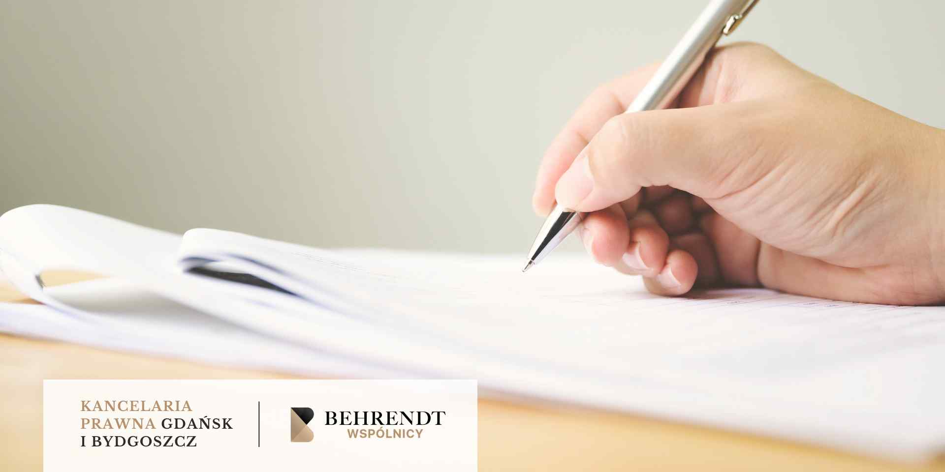 <br />
Zbliżenie przedstawia dłoń, która trzyma srebrny długopis i pisze na dokumencie leżącym na drewnianym biurku