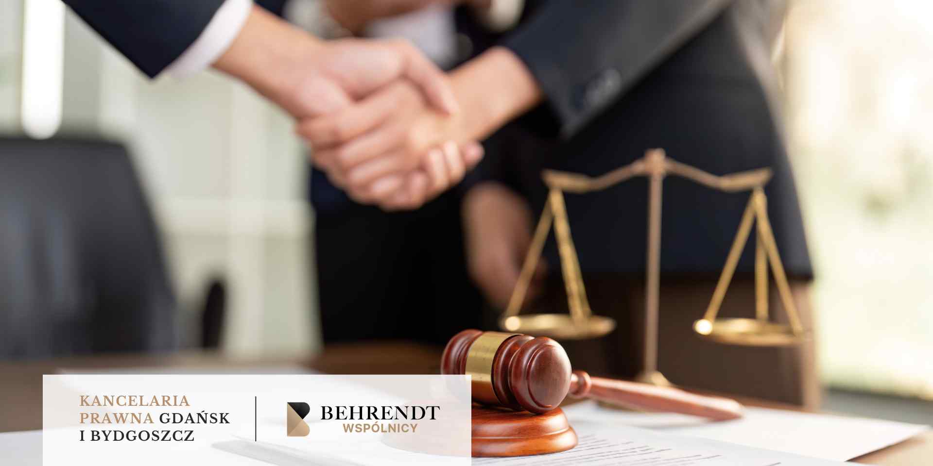Zbliżenie na uścisk dłoni dwóch mężczyzn w garniturach, z wagą sprawiedliwości i młotkiem sędziowskim leżącymi na stole w tle, co symbolizuje porozumienie lub zakończenie sprawy prawnej.