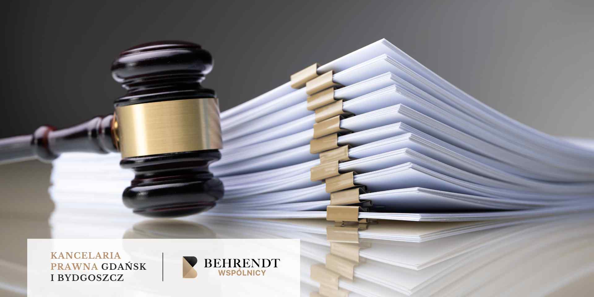 Duży stos dokumentów zabezpieczony złotymi spinaczami biurowymi leży obok drewnianego młotka sędziowskiego z metalowym okuciem