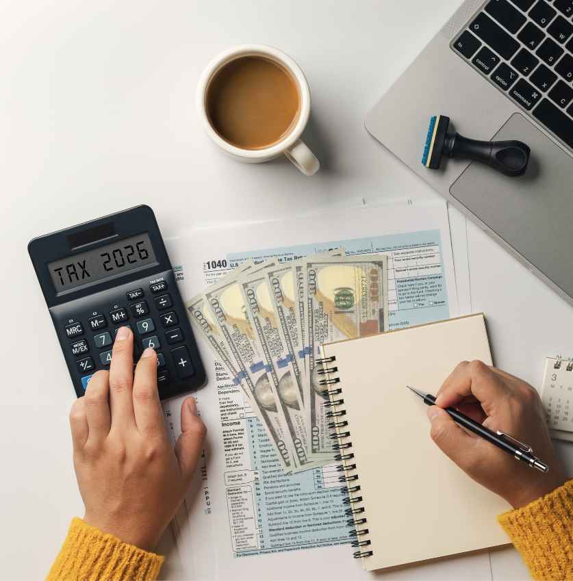 Widok z góry na ręce osoby wypełniającej formularz podatkowy 1040 przy użyciu kalkulatora z napisem „TAX 2026”, obok filiżanki kawy i gotówki w dolarach.