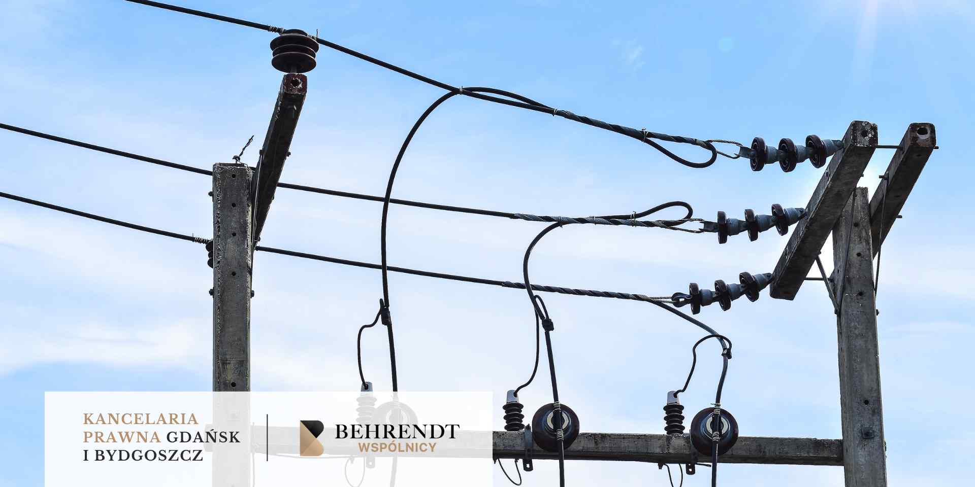 Detal górnej części betonowego słupa energetycznego z rozbudowaną infrastrukturą przewodów i izolatorów na tle jasnego nieba.