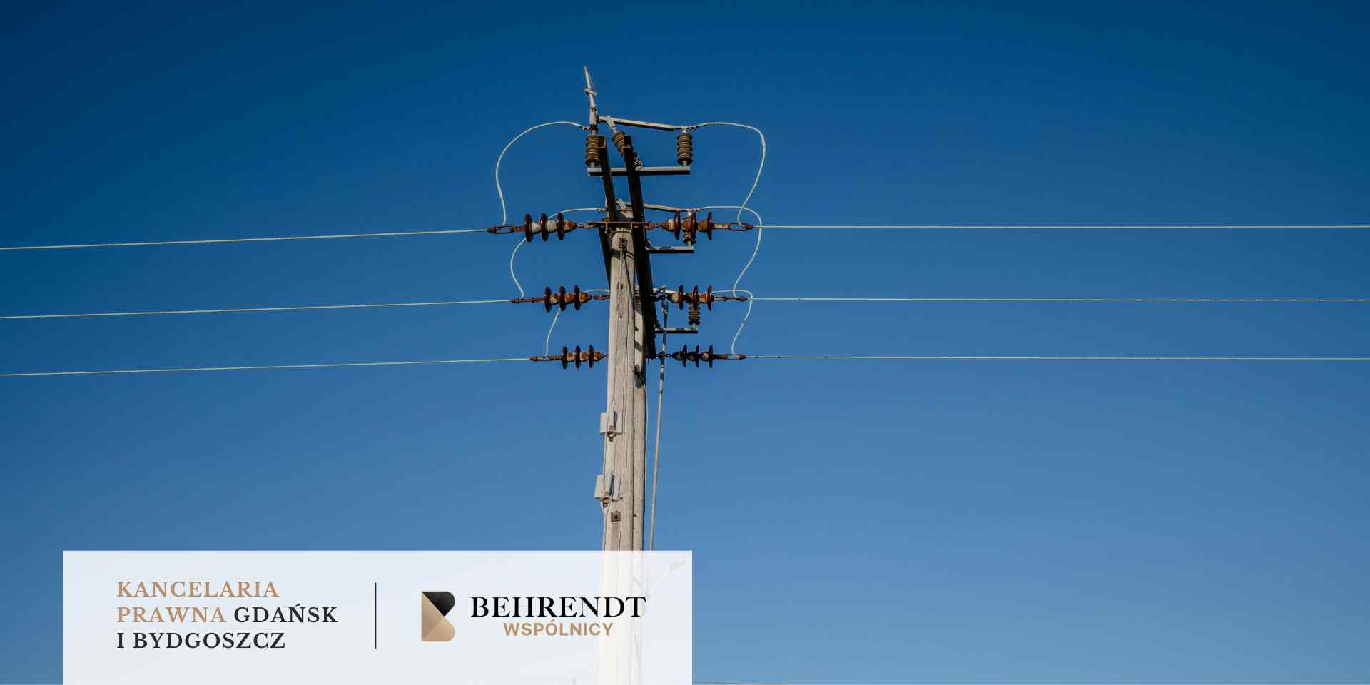 Betonowy słup wysokiego napięcia z rozbudowaną konstrukcją izolatorów i poziomymi liniami energetycznymi na tle czystego, intensywnie niebieskiego nieba.