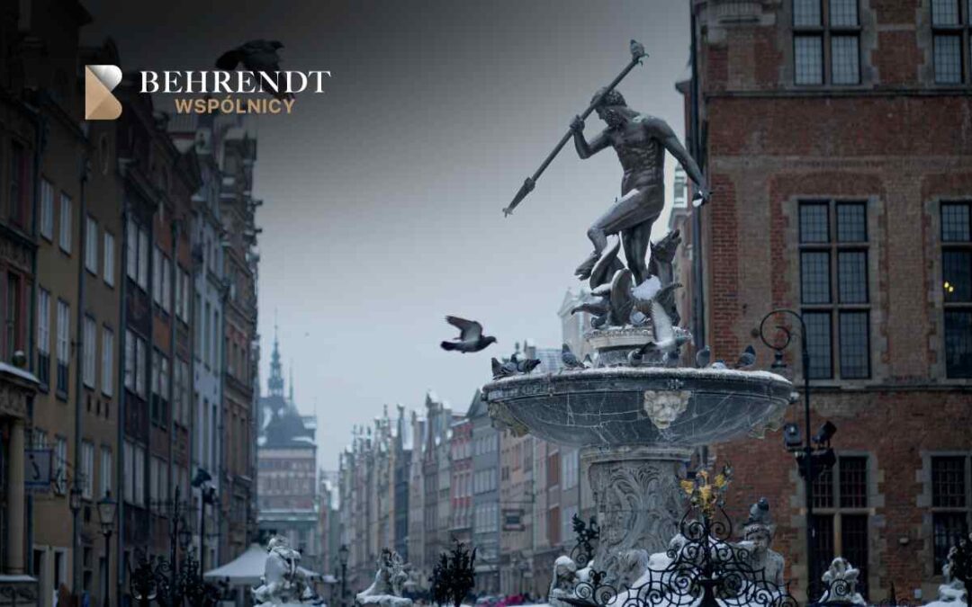 Malowniczy widok na Fontannę Neptuna w Gdańsku na tle zabytkowych kamienic Długiego Targu w zimowej lub chłodnej aurze. Rzeźba Neptuna oraz czasza fontanny są lekko przyprószone śniegiem, a wokół latają gołębie.