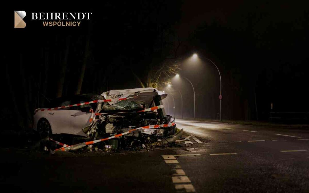 White car damaged in a nighttime crash on a dim street, taped off with orange-and-white barrier tape; Behrendt Wspólnicy logo in the top-left corner.