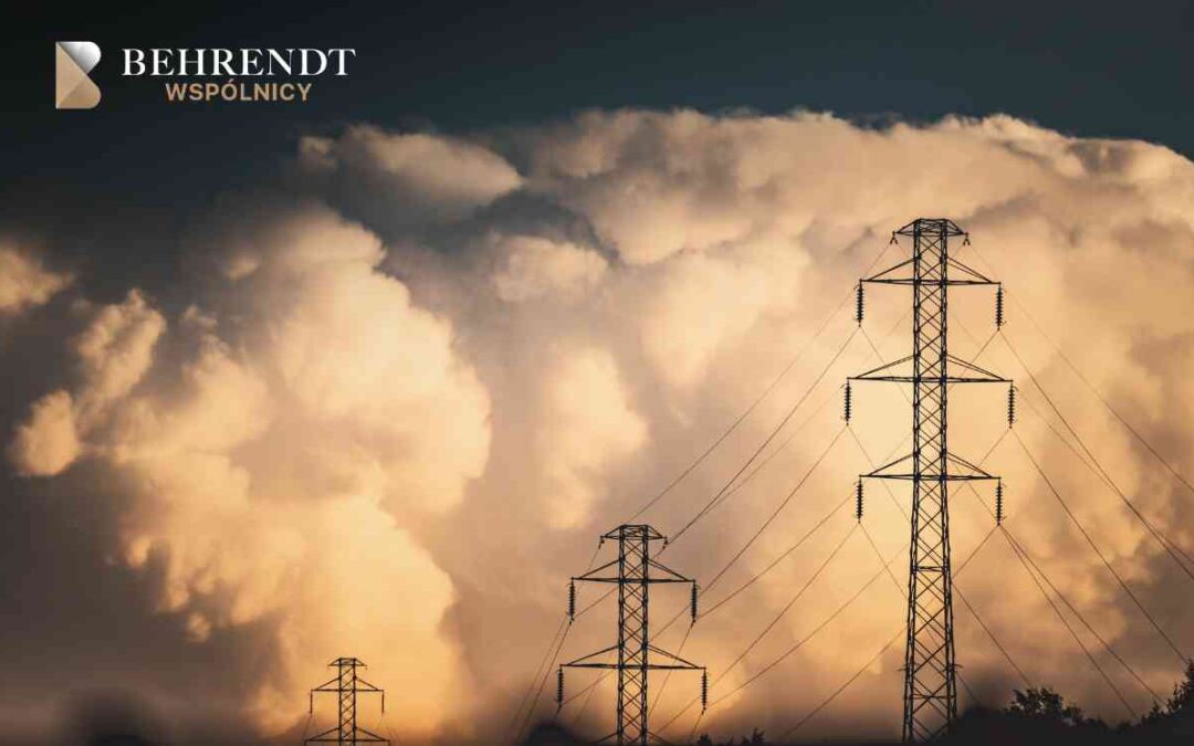 Trzy stalowe słupy linii wysokiego napięcia na tle kłębiących się, ciemnych chmur burzowych oświetlonych zachodzącym słońcem.