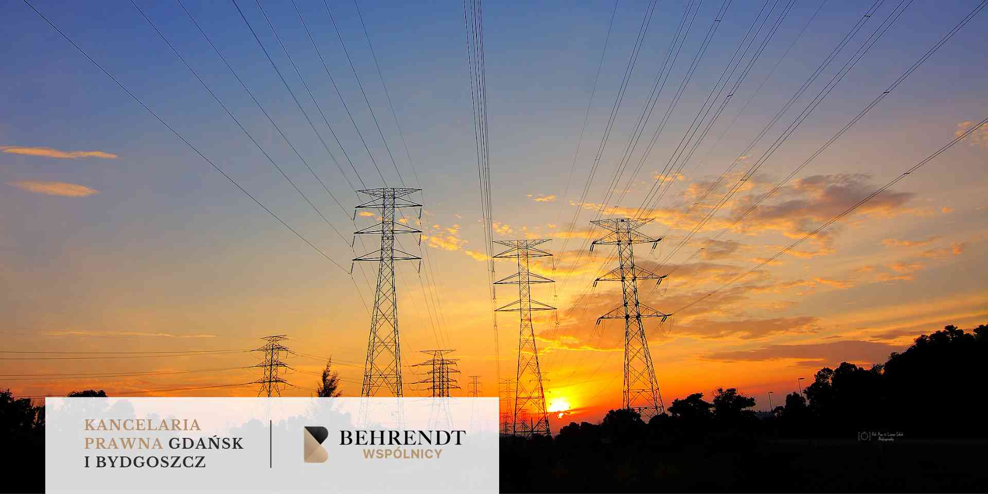 Szereg stalowych słupów energetycznych i liczne linie wysokiego napięcia ciągnące się nad horyzontem w stronę zachodzącego słońca; niebo w odcieniach złota i błękitu.