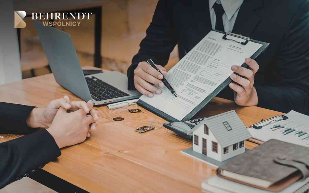 Two professionals sign a contract at a wooden desk, with a small house model, laptop, and documents nearby; Behrendt Wspólnicy logo visible.