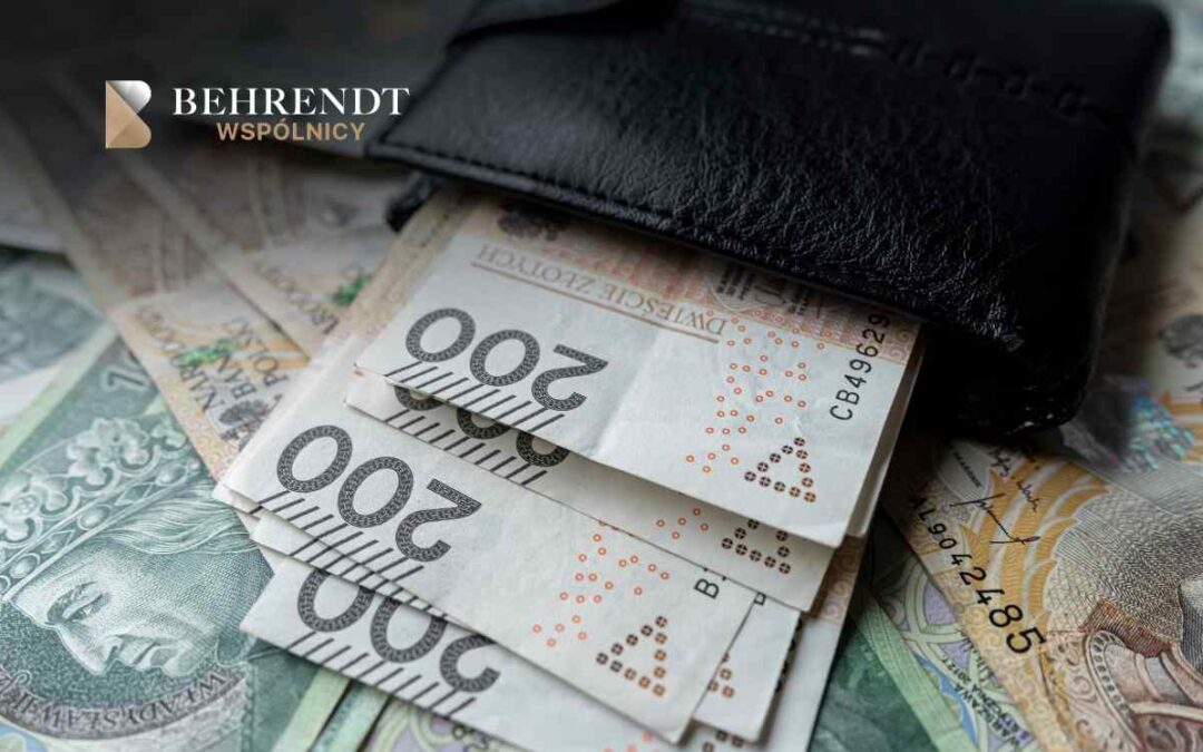Zbliżenie na czarny skórzany portfel, z którego wystają polskie banknoty o nominale 200 zł, leżące na rozsypanych pieniądzach. W lewym górnym rogu znajduje się logotyp Kancelarii Behrendt Wspólnicy.