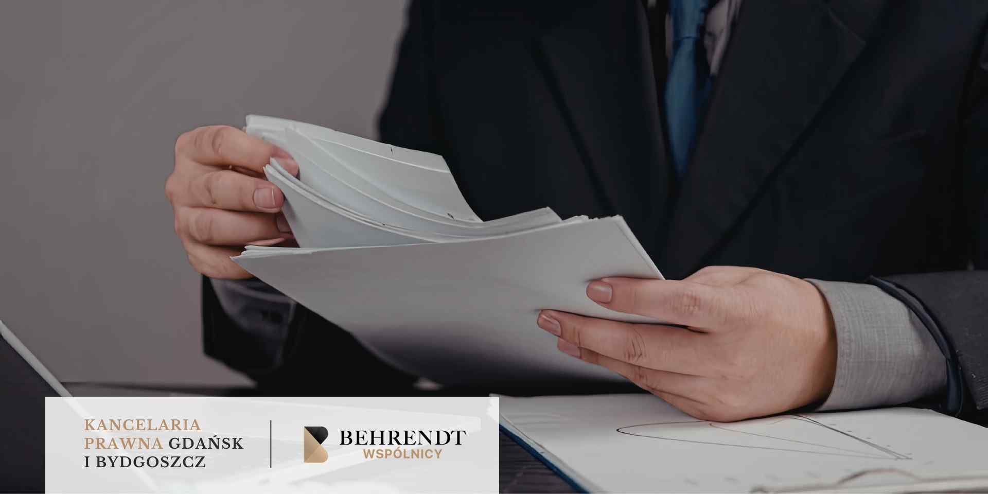 Osoba w ciemnym garniturze przegląda plik białych dokumentów trzymanych w dłoniach.