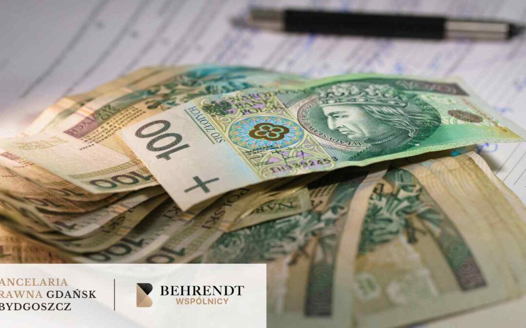 Plik banknotów o nominale 100 złotych polskich (PLN) leżący na wypełnionych dokumentach i formularzach; w tle widoczny jest czarny długopis.