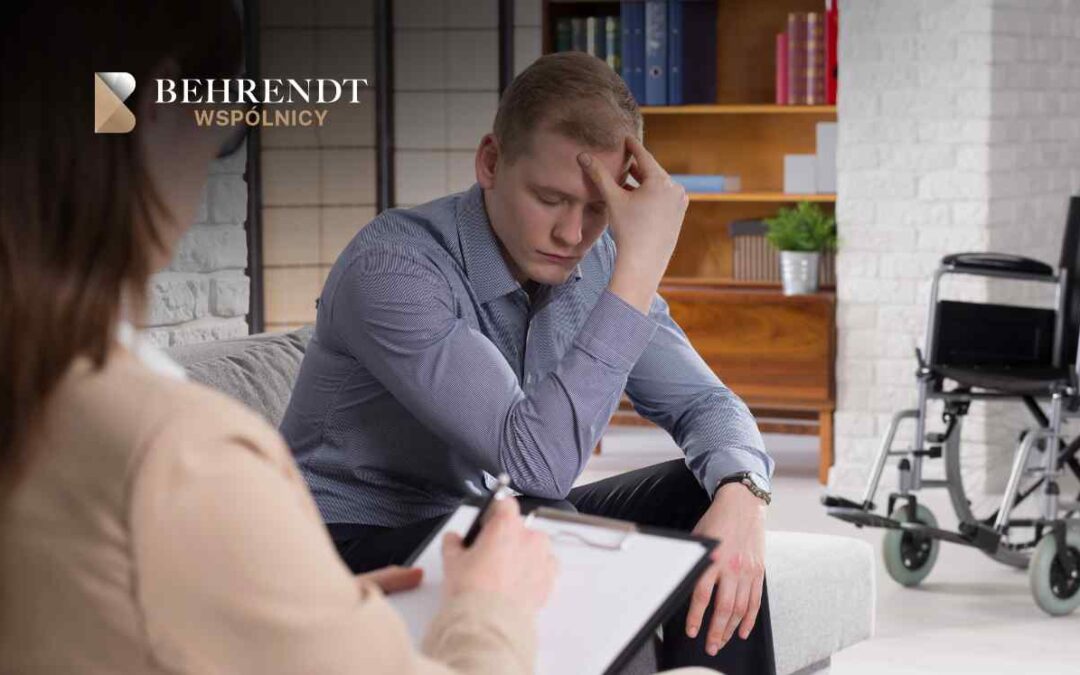 Młody mężczyzna siedzi na kanapie z opuszczoną głową, trzymając się za czoło w geście rezygnacji lub bólu; naprzeciwko niego siedzi prawnik z podkładką i dokumentami, sporządzając notatki. W tle widoczny jest wózek inwalidzki.