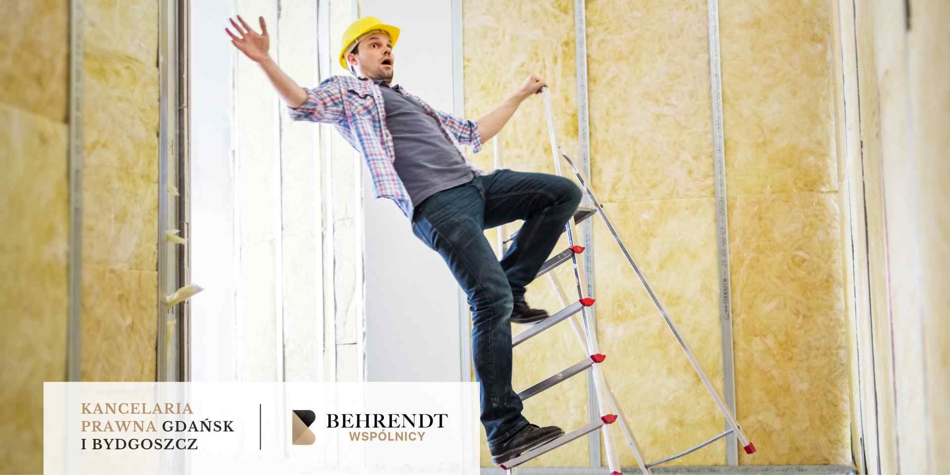 Mężczyzna w żółtym kasku ochronnym traci równowagę i spada z aluminiowej drabiny podczas prac remontowych wewnątrz budynku, na tle ścian wyłożonych wełną mineralną.