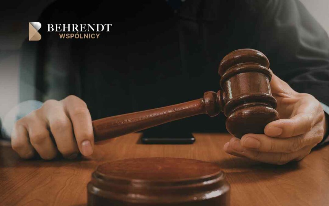 Zbliżenie na dłonie sędziego trzymające drewniany młotek oparty o stół, tuż przed ogłoszeniem orzeczenia.