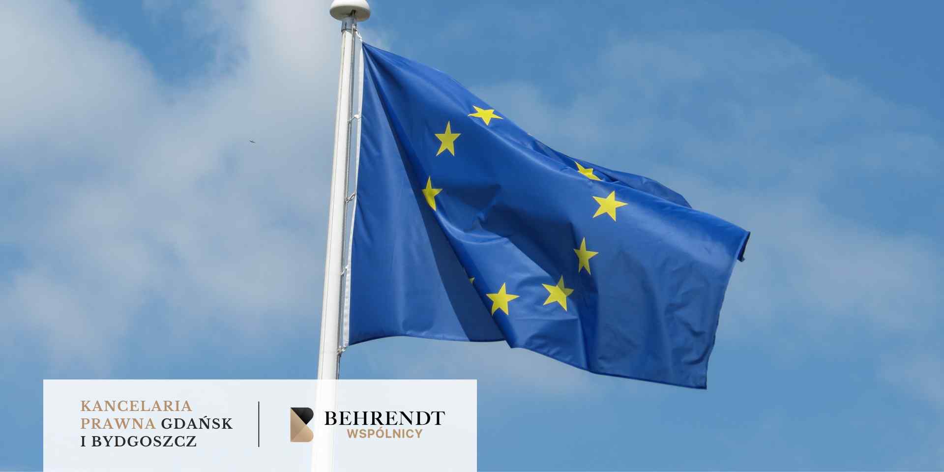 Flaga Unii Europejskiej z żółtymi gwiazdami na niebieskim tle, powiewająca na maszcie na tle błękitnego nieba z lekkimi chmurami.