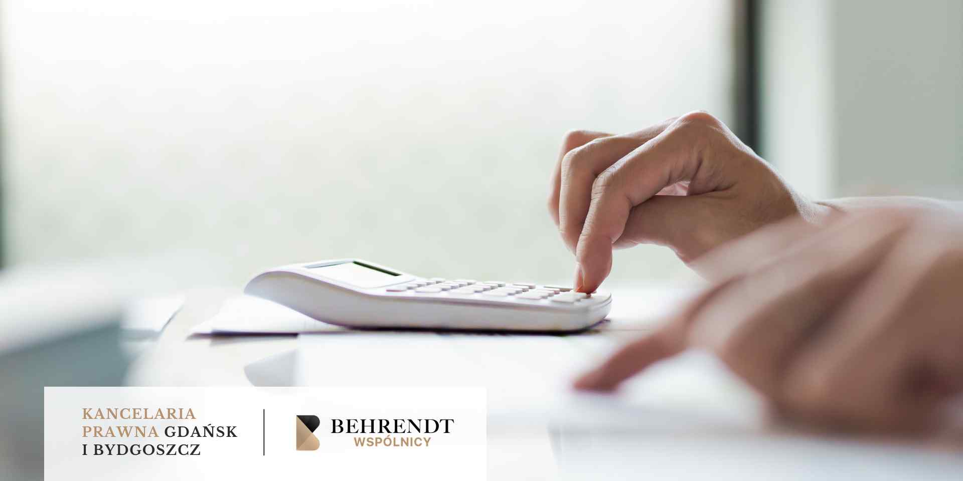 Zbliżenie na dłonie osoby obsługującej biały kalkulator biurowy na jasnym blacie; tło jest miękko rozmyte.