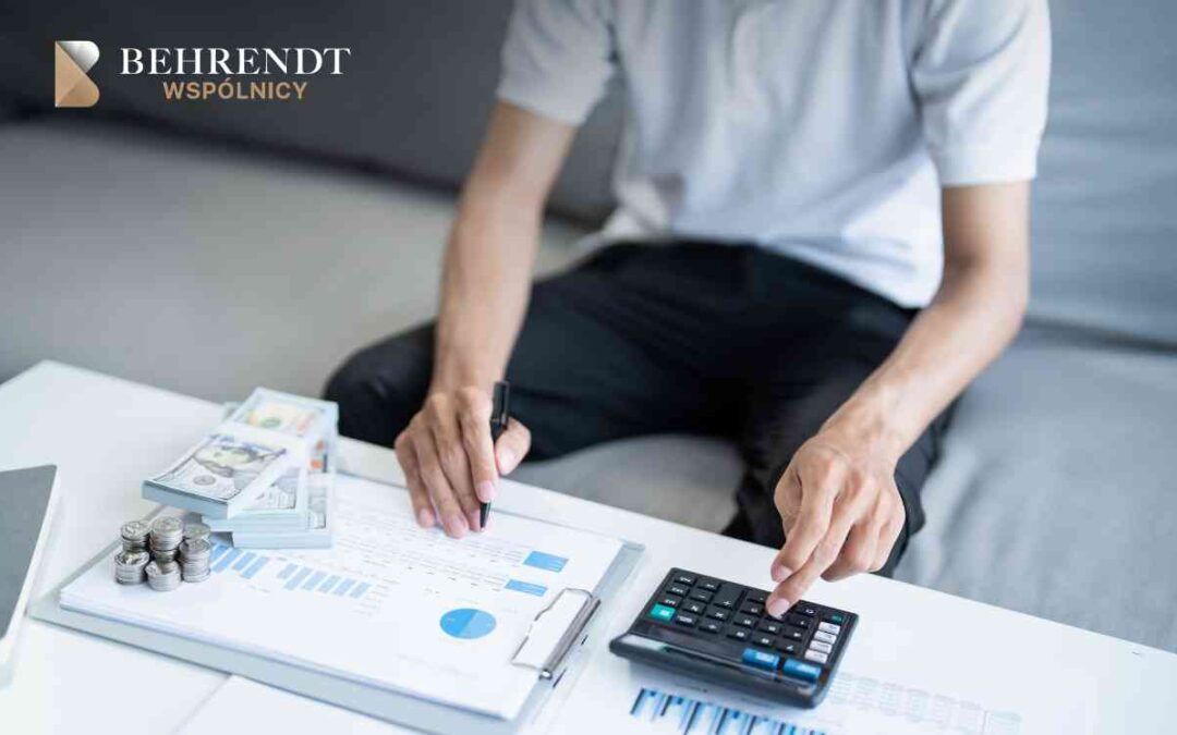 Man calculating finances at a white desk with charts, stacks of cash, and a calculator; company logo in the top-left corner.