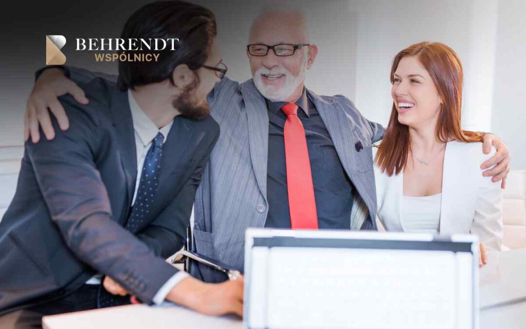 Three business professionals smiling and leaning together at a desk, Behrendt WSPÓLNICY logo visible in the top left corner.