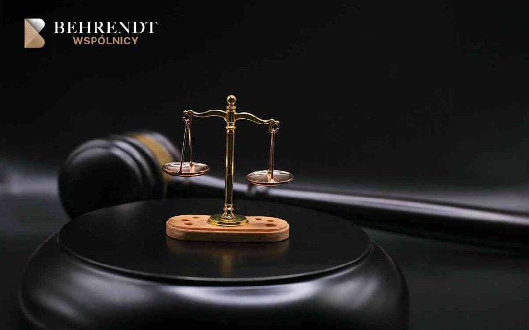 Gold scales of justice on a wooden base with a gavel and dark backdrop; Behrendt Wspólnicy branding in the top-left corner.