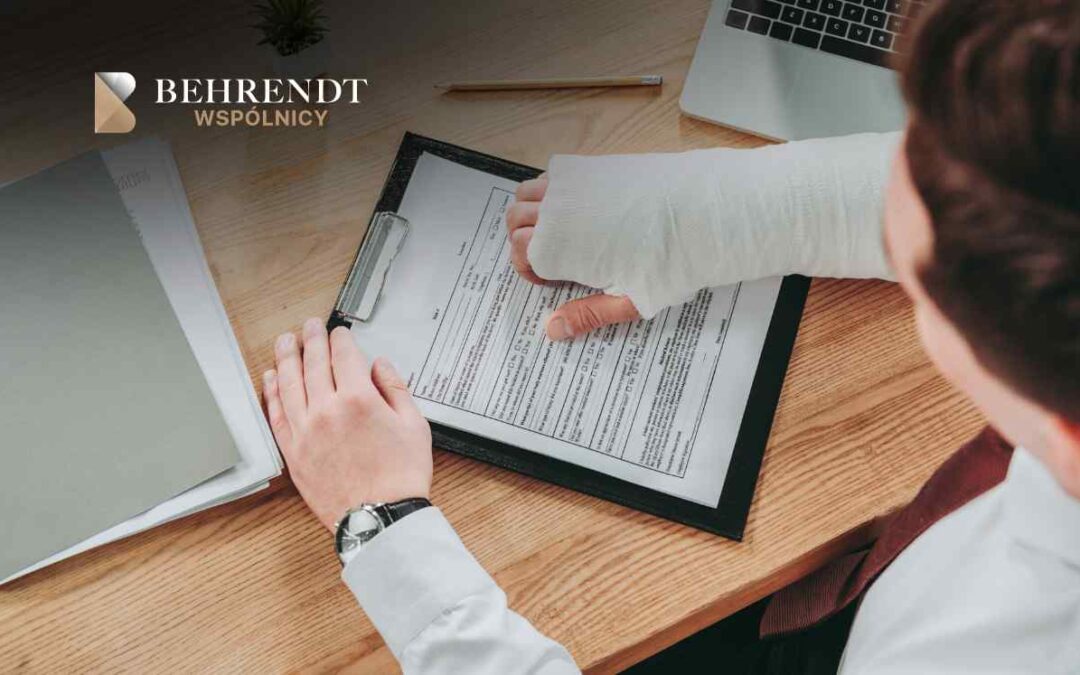 Person with a cast signs a document on a clipboard at a wooden desk, Behrendt Wspólnicy logo visible in the corner