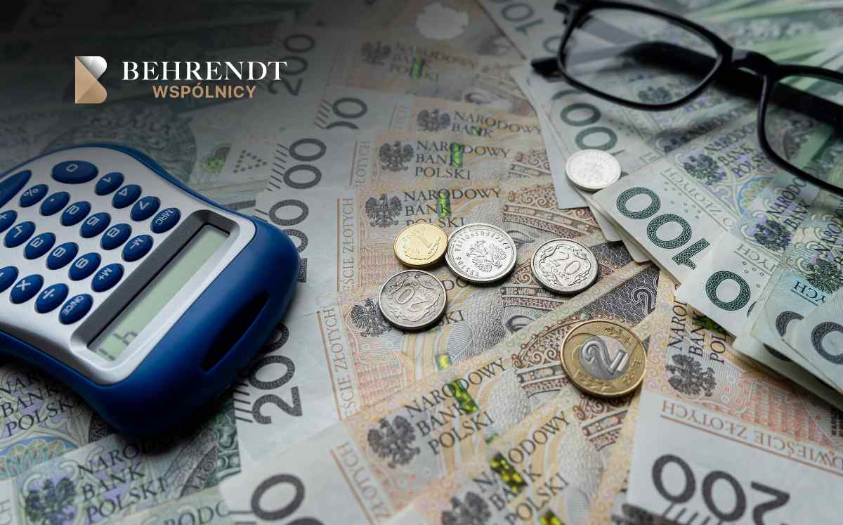 Polish zloty banknotes and coins scattered around a blue calculator with a pair of glasses and the Behrendt WSPÓLNICY logo in the corner, suggesting financial planning or accounting.