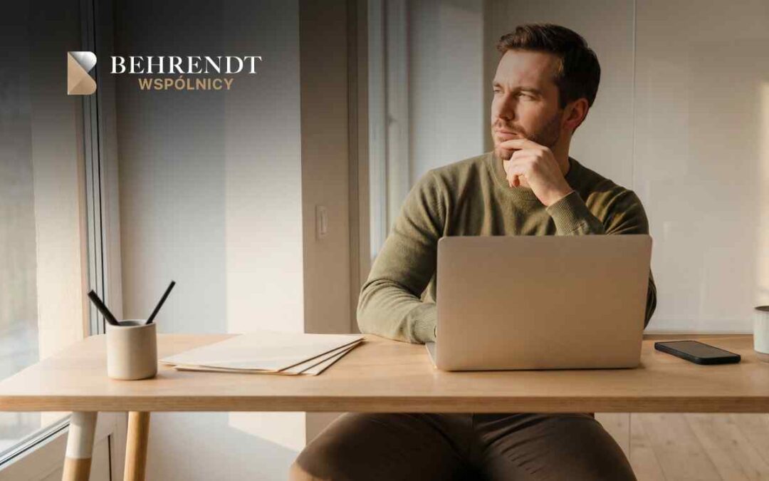 Man at a wooden desk with an open laptop, looking thoughtful; logo 'BEHRENT WSPÓLNICY' visible in the background.