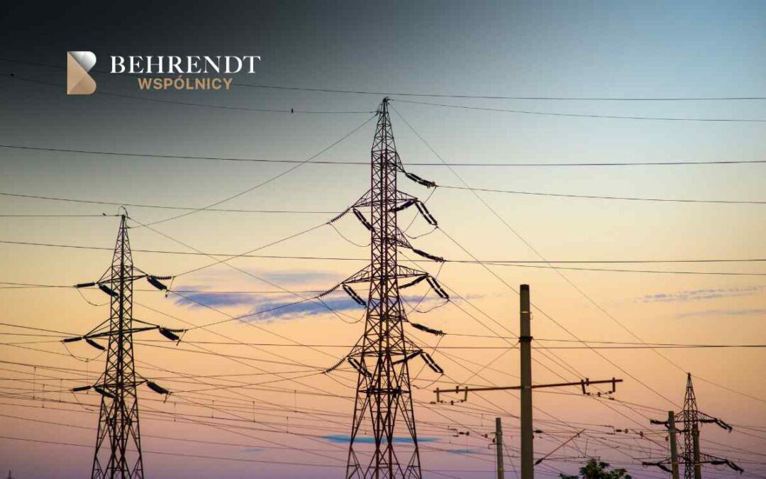 Sunset over a network of electrical pylons and wires, with the Behrendt Wspólnicy logo in the upper left corner.