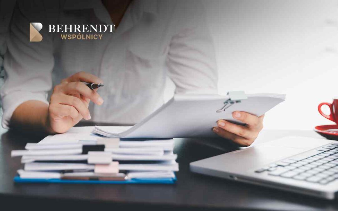 Professional reviewing documents at a desk with a laptop; logo in the top-left corner.