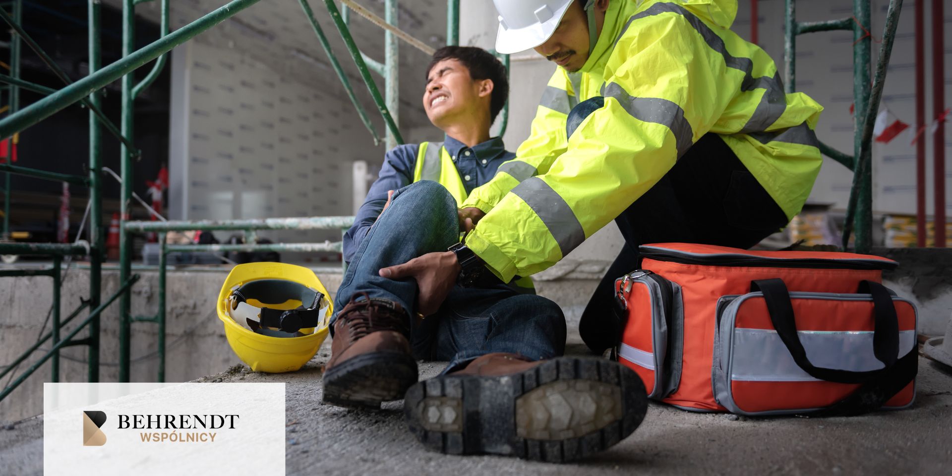 Construction site scene: a worker in a neon safety jacket tends to a seated coworker, with a yellow hard hat and a red medical bag nearby.