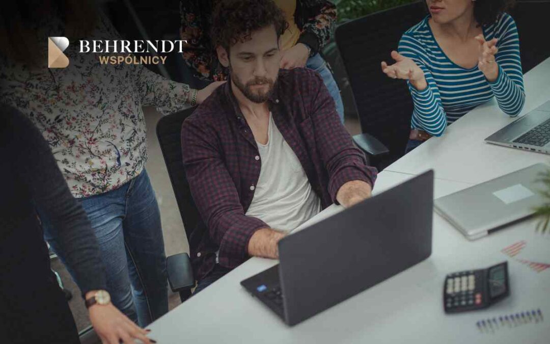 Team of professionals gathered around a laptop on a white conference table, Behrendt Wspólnicy logo visible in the top-left corner.