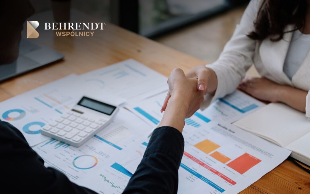 Handshake over financial reports and a calculator on a wooden table, with a company logo in the top-left.