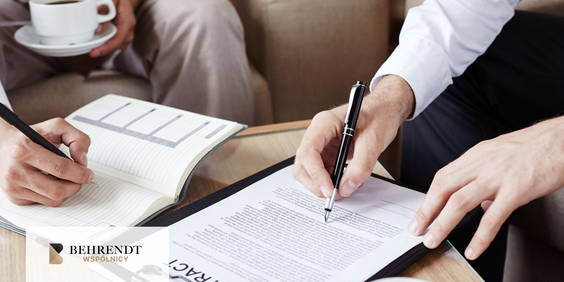 Lawyer's hand with ring rests on a desk during a meeting, with documents and a gavel nearby and a firm logo in the corner.